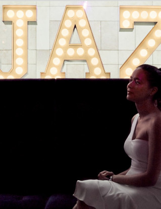 Close-up of a woman sitting in front of a huge, illuminated “Jaz” lettering.