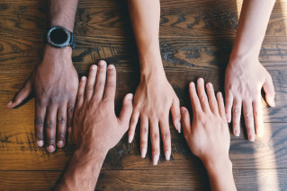 Image detail of five different persons' hands on a wooden background.