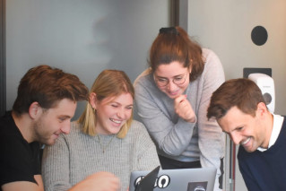 Four happy young people working together on a laptop.