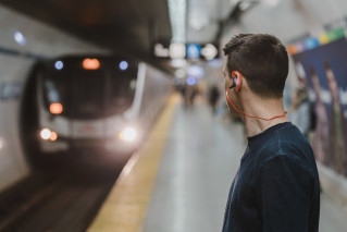 A young person standing on a platform. A modern subway is just pulling in.