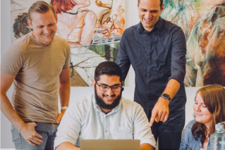 A diverse group of people working together on a laptop.