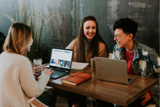 Three young people sitting together at a table, working on their laptops.