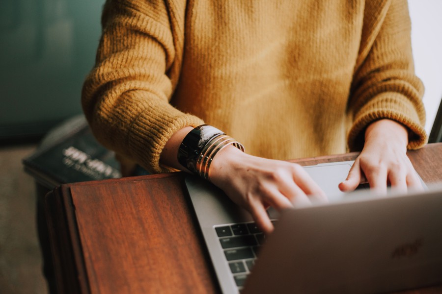 Close-up on the hands and arms of a young person, working on a laptop.