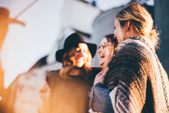 Three young, laughing people in close-up. The evening sun is shining on their faces.