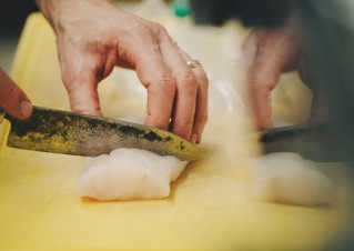 Detailaufnahme einer Hand, die mit einem scharfen Messer Fisch schneidet.