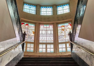 Ein beeindruckendes Treppenhaus. Die hohen Fenster sind mit bunten Glaseinsätzen versehen.